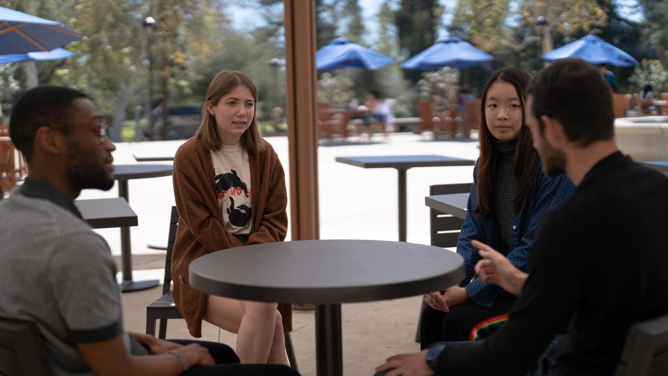 four speaking partners sitting at a table together, talking